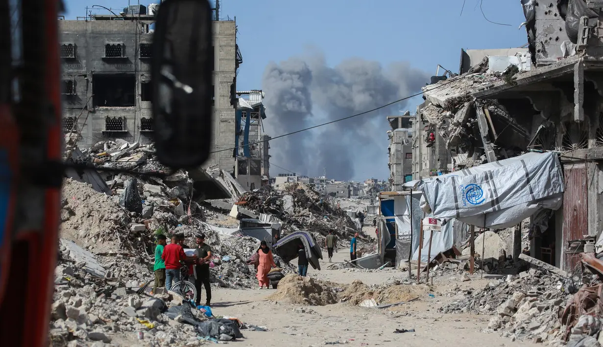 Asap mengepul ke arah utara menjadi latar ketika warga Palestina bergerak melalui Jabalia meninggalkan Jalur Gaza utara menuju Kota Gaza pada 19 Mei 2025. (Bashar TALEB/AFP)
