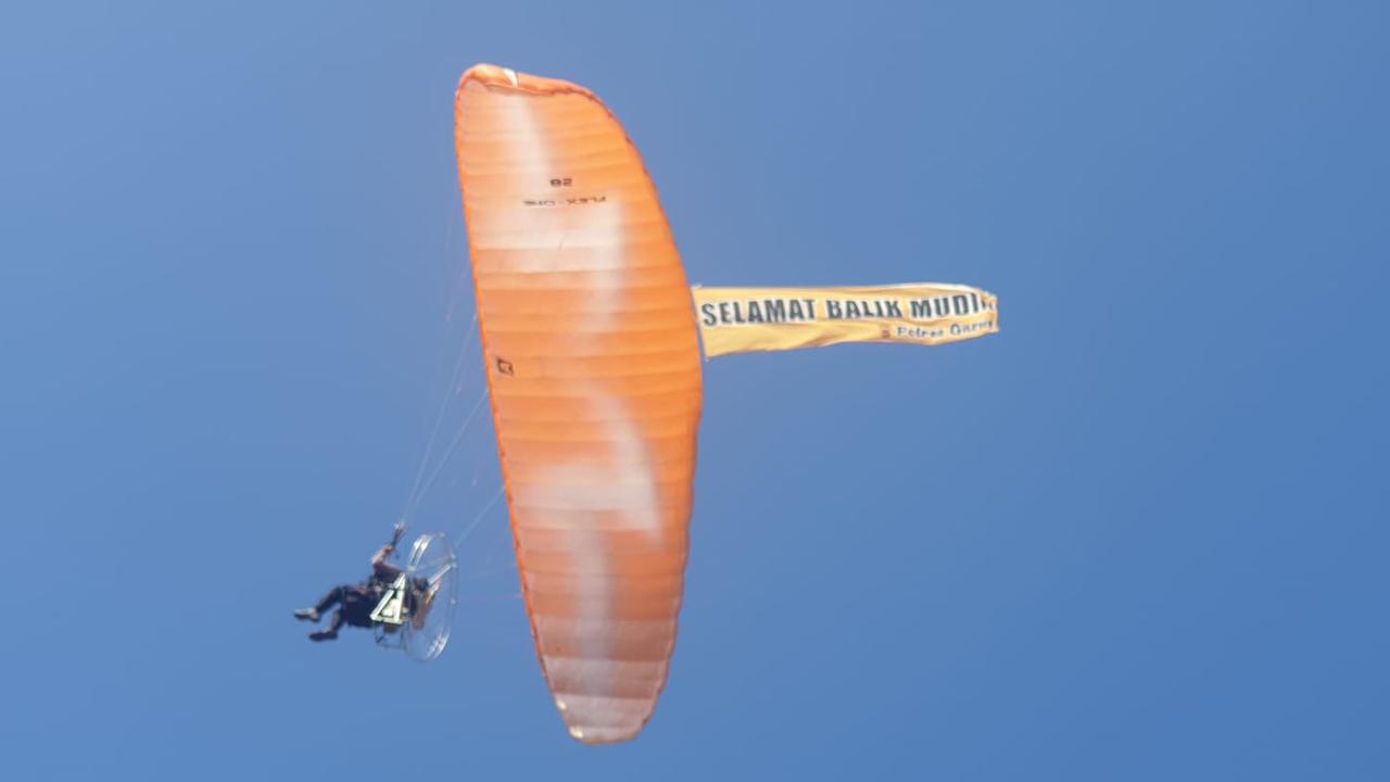 Seorang anggota polres Garut, Jawa Barat nampak lihat menerbangkan parasit paramotor sambil memebentangkan spanduk himbauan mudik lancar. (Liputan6.com/Jayadi Supriadin)