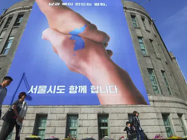 Pejalan kaki berjalan melewati spanduk yang menunjukkan foto dua tangan bersalaman dengan gambar peta Semenanjung Korea di Seoul, Korea Selatan (18/4). Spanduk ini bertujuan untuk mendukung pertemuan antara Korut dan Koresel. (AFP Photo/Jung Yeon-je)