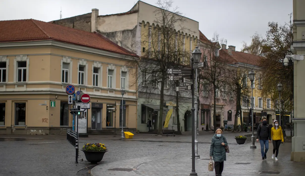 Penduduk lokal berjalan di Kota Tua yang kosong di Vilnius, Lithuania (7/11/2020). Seluruh wilayah telah dikunci selama tiga minggu secara nasional dari 7 November hingga 29 November, yang memberlakukan pembatasan pada kehidupan sosial dan kegiatan ekonomi.  (AP Photo/Mindaugas Kulbis)