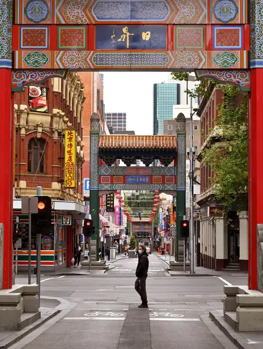 Orang-orang berjalan di jalan yang sepi di Chinatown Melbourne, Australia, Selasa (19/10/2021). Melbourne bersiap mencabut aturan penguncian pekan ini setelah kota tersebut berada dalam enam pekan lockdown selama 262 hari atau hampir sembilan bulan sejak Maret 2020. (William WEST/AFP)