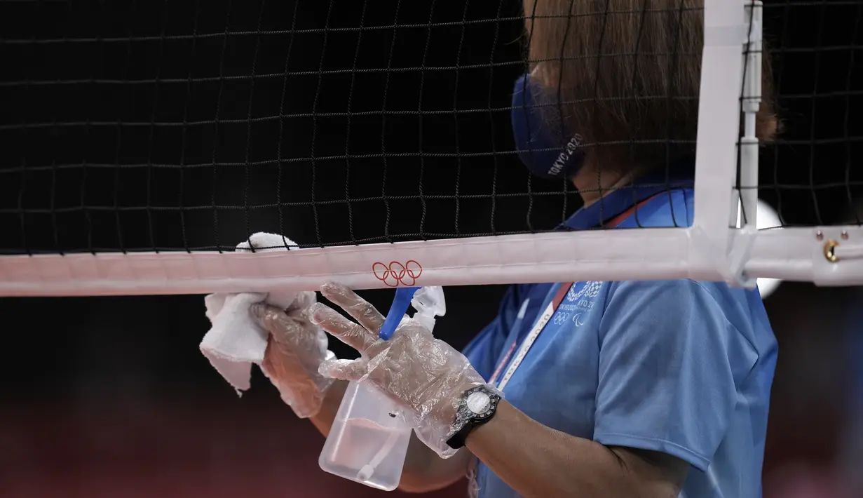 Seorang petugas, mengenakan sarung tangan plastik, menggunakan kain untuk mendisinfektan jaring bola voli sebelum dimulainya pertandingan babak penyisihan grup A bola voli putri Olimpiade Tokyo 2020, pada 25 Juli 2021, di Tokyo, Jepang. (AP Photo/Manu Fernandez)