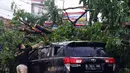 Seorang pria membersihkan dahan pohon tumbang yang menimpa mobil di Kota Tangerang, Banten, Kamis (23/12/2021). Puluhan pohon dan gapura tumbang akibat terjangan angin kencang saat hujan lebat melanda Kota Tangerang. (Liputan6.com/Angga Yuniar)