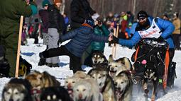 Dallas Seavey membungkuk untuk melakukan high-five saat Iditarod Sled Dog Race di Deshka Landing di Willow, Alaska, Minggu (7/3/2021). Jarak yang harus ditempuh biasanya hampir 1.000 mil dan tahun ini dikurangi menjadi sekitar 100 mil. (Marc Lester/Anchorage Daily News via AP)