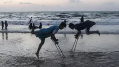 Dua pemuda Palestina Mohammed Eliwa (kiri) dan Ahmed al-Khoudari melakukan pemanasan sebelum bermain sepak bola di pantai di Kota Gaza (20/9/2019). Eliwa 17 tahun dan Ahmed al-Khoudari 20 tahun kehilangan satu kakinya saat bentrok di perbatasan Israel. (AFP Photo/Mahmud Hams)