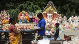 Seorang anak membantu orangtuanya menjual patung Dewa Ganesha di kios pinggir jalan di Hyderabad, India, Kamis (9/9/2021). Patung dewa Hindu berkepala gajah tersebut banyak dijual jelang Festival Ganesh Chaturthi. (NOAH SEELAM/AFP)