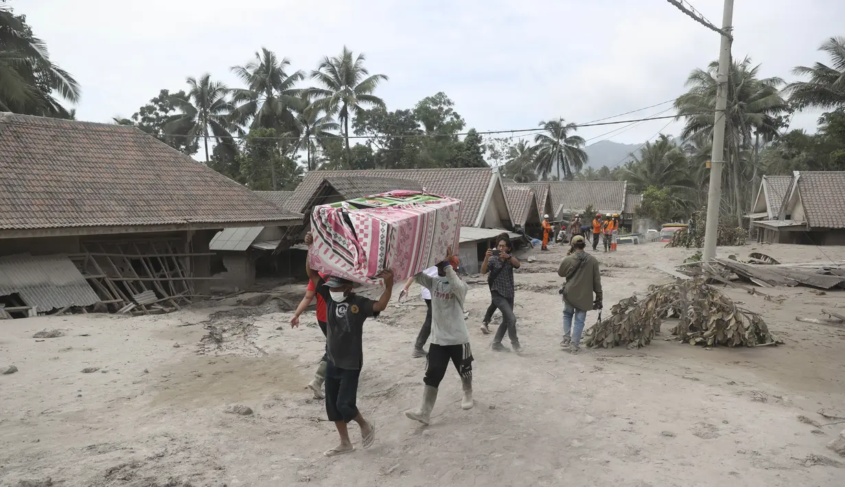 Warga membawa barang bawaannya saat mengungsi ke tempat yang lebih aman pasca erupsi Gunung Semeru di Kabupaten Lumajang, Provinsi Jawa Timur, Minggu (5/12/2021). (AP Photo/Trisnadi)