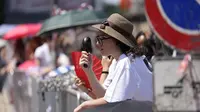 Sejumlah orang berupaya menyejukkan diri saat menunggu kedatangan para tamu pada peragaan koleksi busana pria Prada Spring/Summer 2027 di Milan, Italia, Minggu (21/6/2026). (Dok. Luca Bruno/AP)
