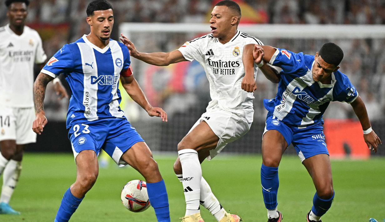 Penyerang Real Madrid, Kylian Mbappe (tengah) berebut bola dengan Alvaro Mourino dan Carlos Benavidez (Alaves) selama pertandingan sepak bola Liga Spanyol di stadion Santiago Bernabeu, Madrid, Selasa 24 September 2024 atau Rabu (25/9/2024) dini hari WIB. (JAVIER SORIANO/AFP)