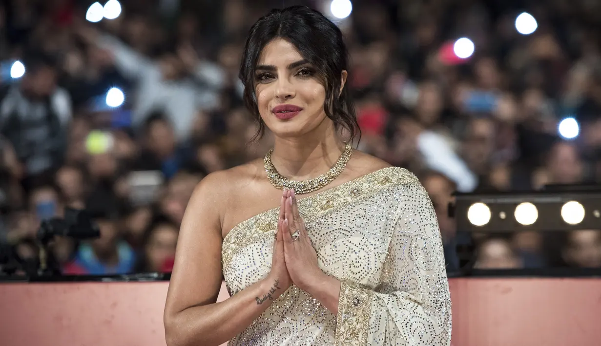 Aktris Priyanka Chopra menyapa penggemarnya saat tiba menghadiri Festival Film Internasional Marrakech ke-18 di Jemaa El Fnaa, Marrakech (5/12/2019). Priyanka Chopra tampil cantik memesona mengenakan busana sari emas dan brokat perak denga dengan kalung emas di lehernya. (AFP/Fadel Senna)