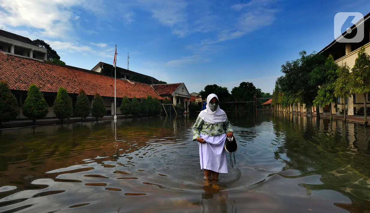 Siswi berjalan melewati banjir yang menggenangi halaman  sekolah di SMAN 4 Tangsel, Pondok Ranji, Tangerang Selatan, Banten, Selasa (14/6/2022). Tiga  pekan lebih banjir merendam lapangan sekolah itu dikarenakan tertutupnya saluran air oleh sampah yang berasal dari tempat pembuangan sampah (TPS) ilegal. (merdeka.com/Arie Basuki)