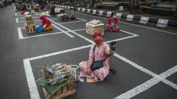 Pedagang menunggu pembeli di dalam garis petak-petak untuk menerapkan jaga jarak (physical distancing) di sepanjang jalan di Surabaya, Selasa (2/6/2020). Garis petak-petak bagi pedagang itu sebagai langkah pencegahan penyebaran COVID-19. (Photo by Juni Kriswanto / AFP)