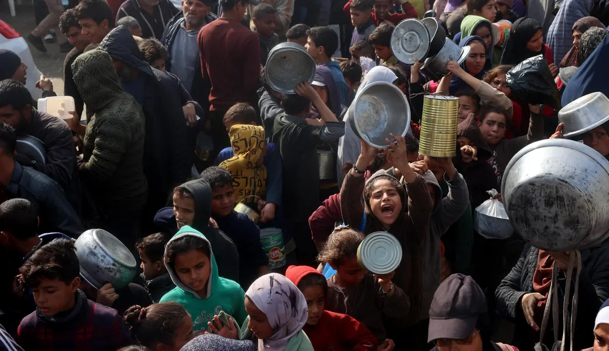 Warga, termasuk anak-anak pengungsi Palestina berkumpul untuk menerima bantuan makanan yang didistribusikan di Deir al-Balah, Jalur Gaza tengah pada 16 Januari 2025. (Eyad BABA/AFP)