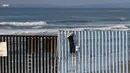 Seorang warga sedang mengecat pagar perbatasan antara Meksiko dan Amerika Serikat di Playas Tijuana, Meksiko (10/12). Pagar yang sebelumnya terlihat usang dan penuh karat nantinya akan diubah menjadi lebih berwarna. (Reuters/Jorge Duenes)