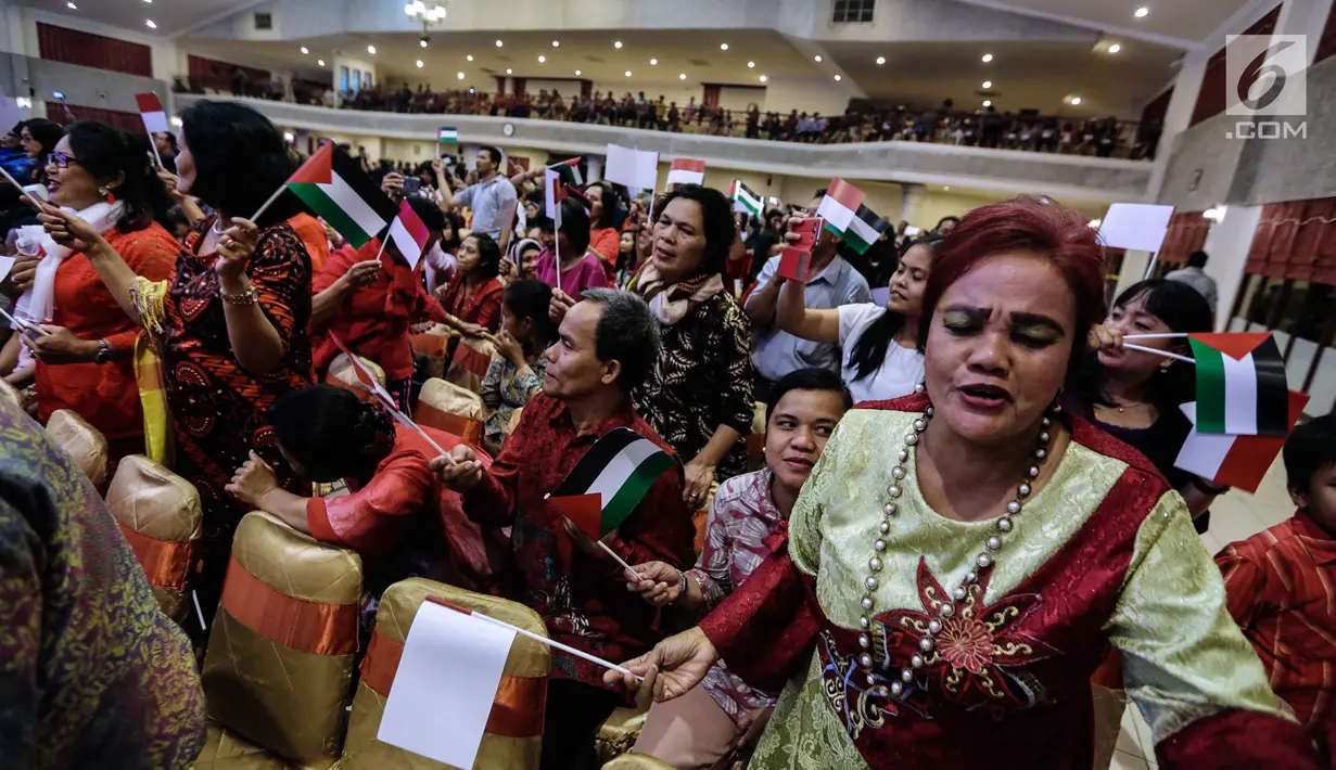 Jemaat mengibarkan bendera merah putih dan Palestina dalam acara Natal Taruna Merah Putih di Jakarta, Jumat (22/12). Perayaan natal tersebut sebagai bentuk kepedulian terhadap kedaulatan Palestina. (Liputan6.com/Faizal Fanani)