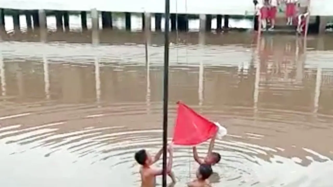 Tiga pelajar SDN 3 Tanah Abang Kabupaten PALI Sumsel mengibarkan bendera di tengah banjir tinggi di lapangan sekolahnya (Liputan6.com / Nefri Inge)