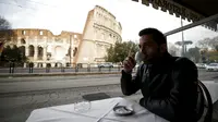 Seorang pria minum kopi di depan Colosseum yang kembali dibuka, Roma, Italia, Senin (1/2/2021). Italia mencabut sebagian langkah pembatasan yang bertujuan untuk menahan penyebaran COVID-19 pada 1 Februari 2021. (Cecilia Fabiano/LaPresse via AP)