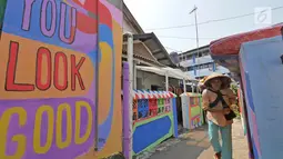 Seorang pedagang melintasi gang sempit yang sisi tembok dindingnya dihiasi lukisan mural warna-warni di Kampung Pejaten, Jakarta, Senin (30/4). Mural motif warna-warni itu digagas warga untuk memperindah kampung mereka. (Liputan6.com/Herman Zakharia)