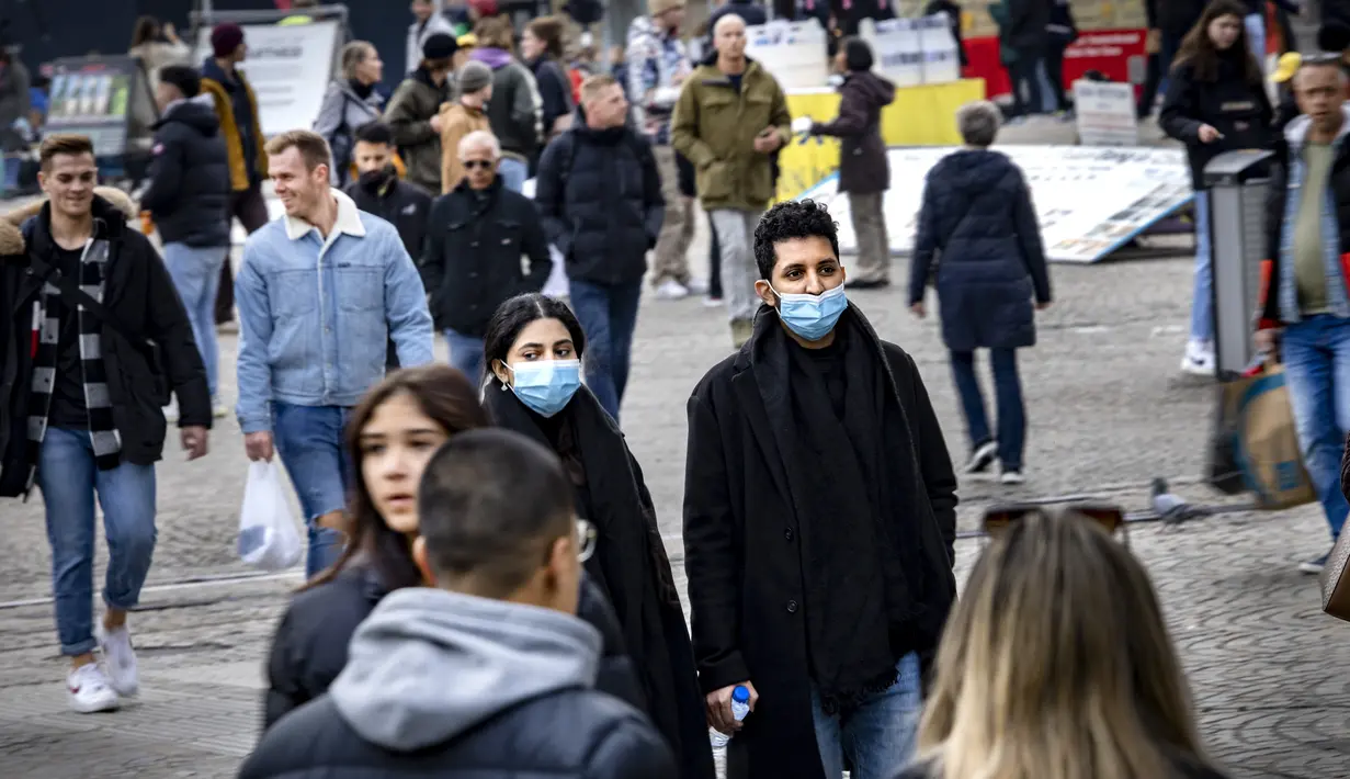Orang-orang dengan masker melintasi jalan di pusat kota Amsterdam, Belanda, Rabu (3/11/2021). Dengan aturan terbaru, pemerintah Belanda mewajibkan penggunaan masker di ruang-ruang publik seperti tempat perbelanjaan, perpustakaan, salon, stasiun kereta, hingga rumah sakit. (Ramon van Flymen/ANP/AFP)