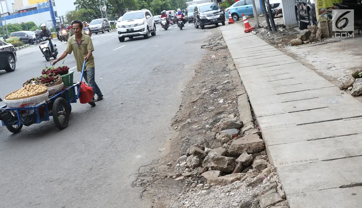 Pedagang melintasi bekas galian gorong-gorong di Jalan Hayam Wuruk, Jakarta, Rabu (20/2). Tidak maksimalnya perbaikan pascapembongkaran gorong-gorong menyebabkan trotoar di kawasan itu rusak dan dipenuhi kerikil serta batu (Liputan6.com/Immanuel Antonius)