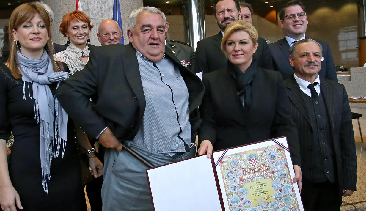 Kepala Komisi HAM Helsinki Kroasia, Ivan Zvonimir Cicak tampak membetulkan celananya yang sempat melorot hingga ke pergelangan kakinya tepat saat sesi foto dengan Presiden Kroasia Kolinda Grabar-Kitrarovic di Zagreb, Selasa (8/12). (STRINGER / AFP)