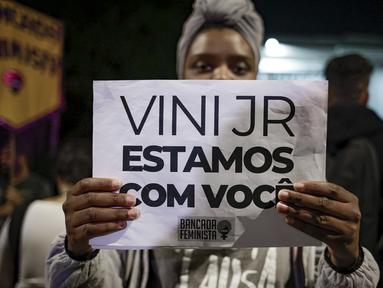Seorang perempuan memegang tanda dengan pesan yang berbunyi dalam bahasa Portugis; "Vini, kami bersamamu," saat memprotes serangan rasis yang dialami pemain Real Madrid asal Brasil, Vinicius Jr., di luar Konsulat Spanyol di Sao Paulo, Brasil, Selasa (23/5/2023). (AP Photo/Tuane Fernandes)