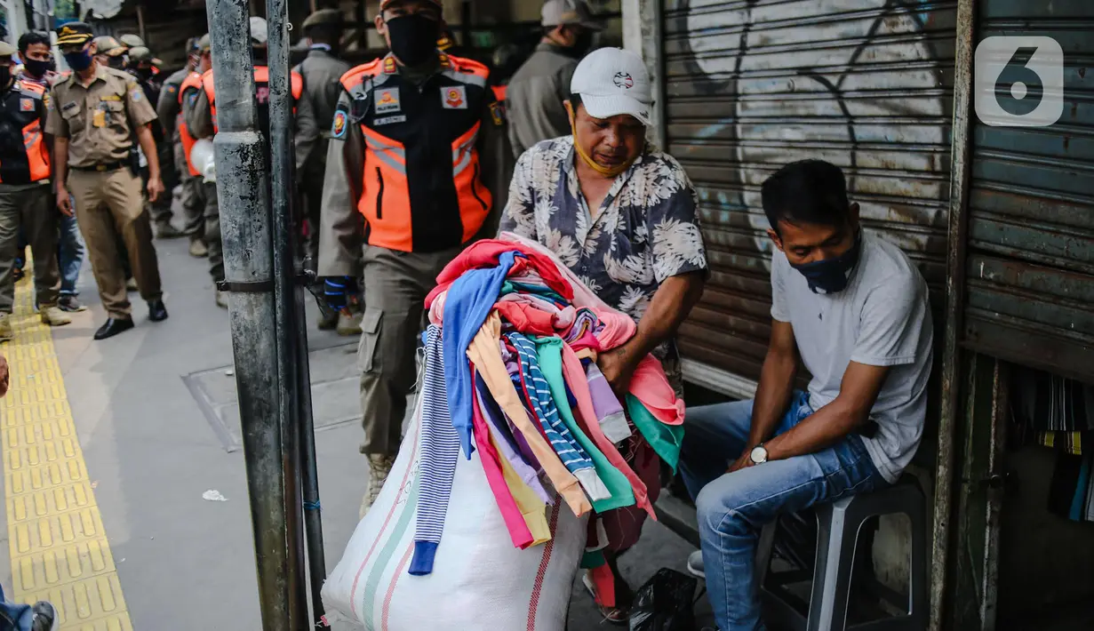 Pedagang membawa pergi dagangannya saat petugas gabungan melakukan penertiban di kawasan Pasar Tanah Abang, Jakarta, Jumat (22/5/2020). Gubernur DKI Jakarta Anies Baswedan menambah PSBB selama 14 hari mulai tanggal 22 Mei 2020. (Liputan6.com/Faizal Fanani)
