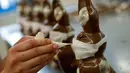 Pekerja menyelesaikan pembuatan cokelat paskah berbentuk kelinci yang mengenakan masker di toko roti Baeckerei Bohnenblust di Bern, Swiss, Jumat (27/3/2020). Di kemasannya dipasang sebuah kertas bertuliskan cara melindungi diri untuk mencegah penularan virus corona. (STEFAN WERMUTH/AFP)