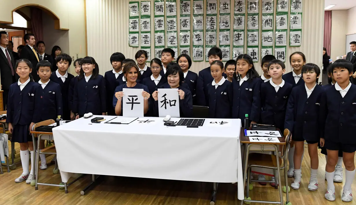 Negara AS Melania Trump (kiri) dan Istri PM Jepang, Akie Abe foto bersama para siswa sambil menunjukkan huruf kanji yang berarti "Damai" saat menghadiri kelas kaligrafi di sekolah dasar Kyobashi Tsukiji, Tokyo (6/11). (AFP Photo/Pool/Toshifumi Kitamura)