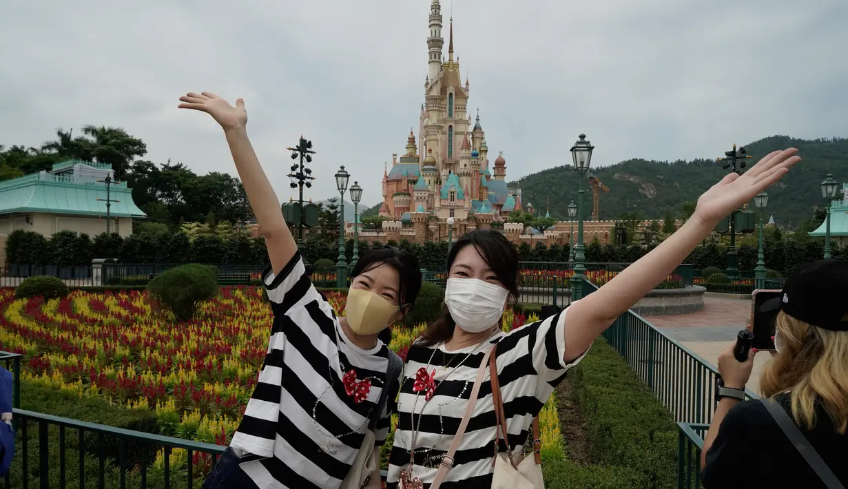 Pengunjung yang mengenakan masker berpose untuk foto di Disneyland Hong Kong pada Jumat (25/9/2020). Setelah dibuka dan tutup kembali, Disneyland Hong Kong dibuka kembali untuk wisatawan. (AP Photo/Kin Cheung)