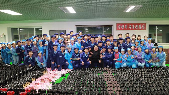 Pemimpin Korea Utara, Kim Jong-Un foto bersama sejumlah pekerja saat mengunjungi pabrik sepatu Wonsan, Korea Utara (3/12). (Photo by KCNA VIA KNS / various sources / AFP)