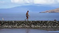 Vicente Ruboi berjalan setelah kebakaran hutan yang melanda Maui di sepanjang tembok laut, di Kihei, Hawaii,  Selasa, 15 Agustus 2023. (AP Photo/Rick Bowmer)