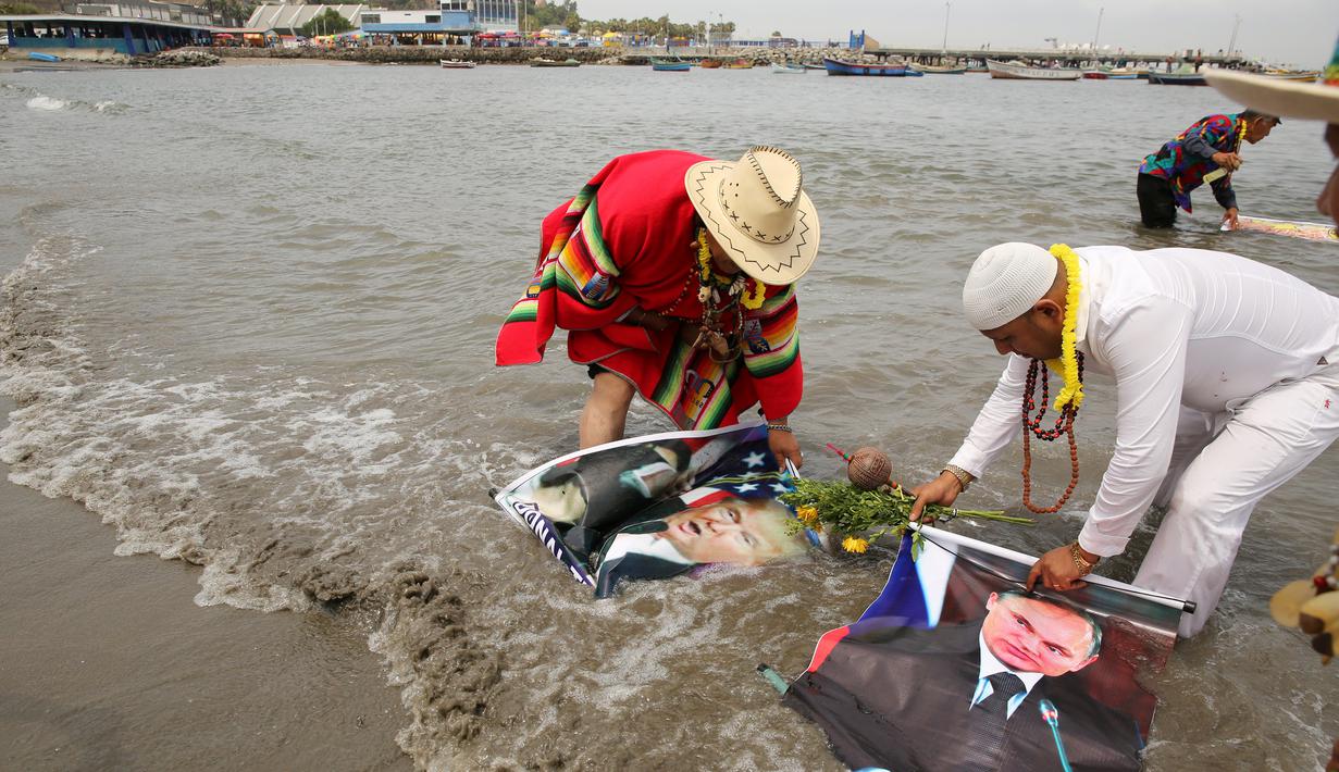 Dukun Peru mencuci poster Presiden Terpilih AS Donald Trump dan Presiden Rusia, Vladimir Putrin saat menggelar ritual di Pantai Agua Dulce di Lima, Peru, (29/12). Dukun tersebut juga meramalkan banyaknya serangan teroris di Eropa. (Reuters/Mariana Bazo)