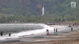 Wisawatan memadati  Pantai Palangpang dengan latar belakang curug di Kecamatan Ciemas, Kabupaten Sukabumi, Selasa (26/6). Pantai Palangpang atau yang biasa disebut Teluk Ciletuh berada di titik utama Geopark Ciletuh-Palabuhanratu (Merdeka.com/Arie Basuki)