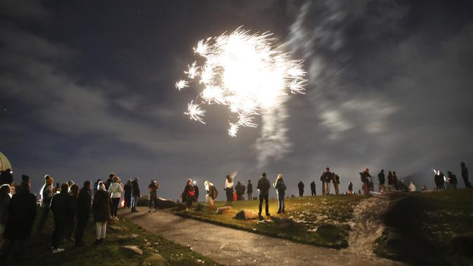 Orang-orang di Calton Hill menonton kembang api di Edinburgh ketika orang-orang didesak untuk menghindari perayaan Hogmanay di tengah pembatasan ketat virus corona pada Kamis, 31 Desember 2020. (Andrew Milligan / PA via AP)