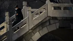 Seorang wanita berjalan melintasi jembatan penyeberangan di taman umum di Beijing, Rabu (5/1/2022). China melaporkan penurunan besar infeksi COVID-19 lokal di kota utara Xi'an, yang telah dikunci ketat selama dua minggu terakhir. (AP Photo/Mark Schiefelbein)