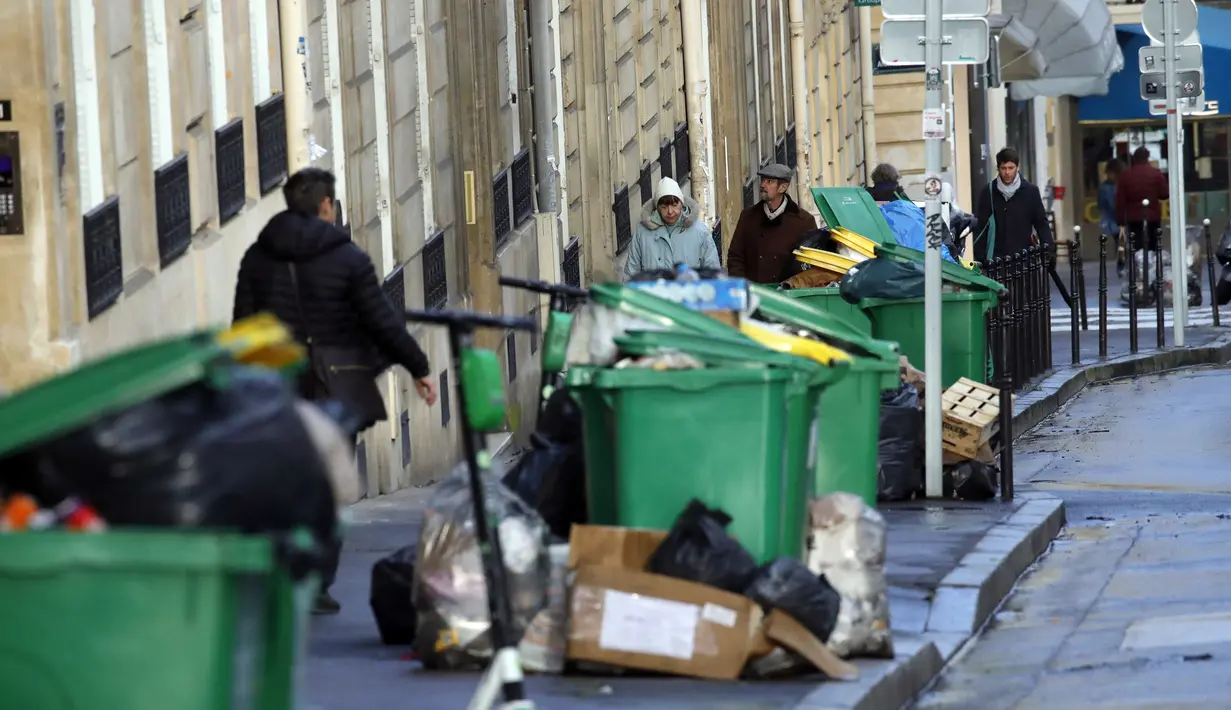 Orang-orang berjalan melewati tong sampah dan tumpukan kantong sampah yang menumpuk di Paris (4/2/2020). Sampah menumpuk di jalan-jalan Paris dan Marseille karena pemogokan perubahan pada sistem pensiun nasional Prancis.  (AP Photo/Christophe Ena)