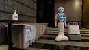Robot Pepper (tengah) dan Whiz (kanan) berdiri di lobi hotel yang diubah menjadi lokasi karantina pasien COVID-19, Tokyo, Jepang, Jumat (1/5/2020). Robot Pepper dan Whiz dikerahkan ke area merah yang memiliki risiko tinggi terinfeksi virus corona COVID-19. (Philip FONG/AFP)