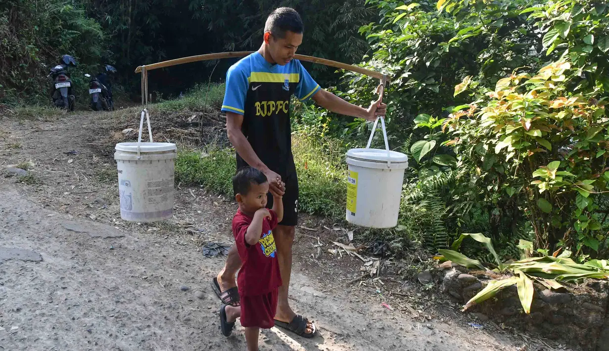 Warga memikul air  yang diambil dari satu-satunya sumber mata air di Kampung Cijaura, Desa Cidokom, Bogor, Jawa Barat, Minggu (26/07/2026). (KLY/ Arie Basuki)