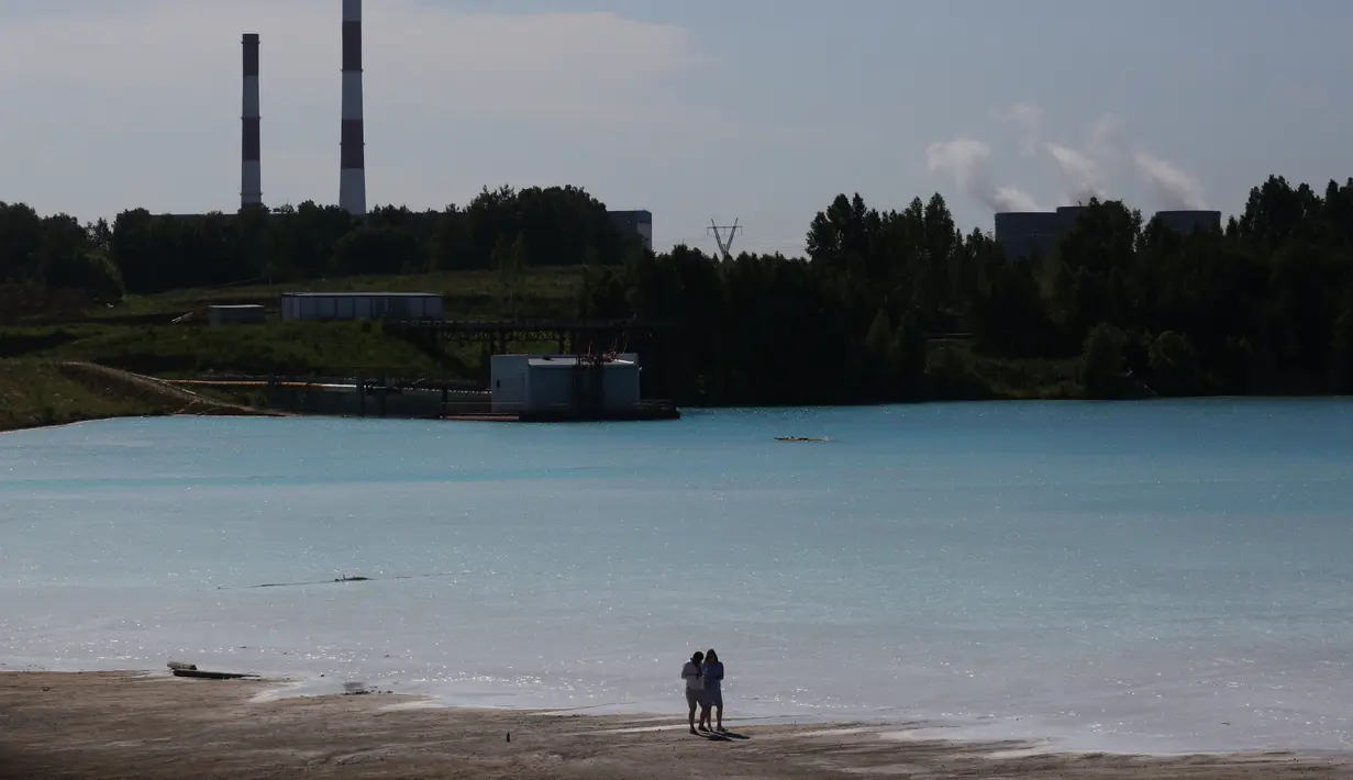 Pasangan berjalan dekat tempat pembuangan abu dari pabrik batubara lokal yang sering disebut 'Maladewa di Siberia' di Danau Novosibirsk, Rusia, Kamis (11/7/2019). Danau buatan yang memiliki hijau muda cerah tersebut kini tengah menjadi viral di media sosial Instagram. (Rostislav NETISOV/AFP)