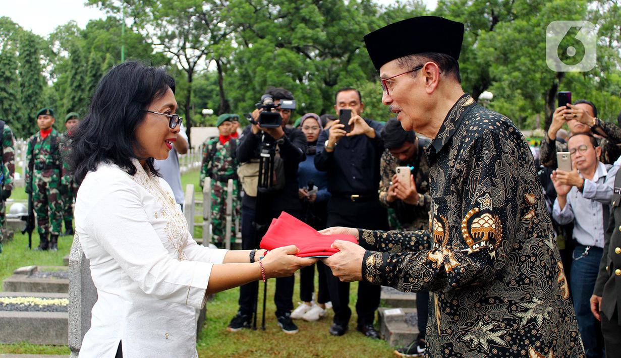 Menteri PPPA, I Gusti Ayu Bintang Darmavati (kiri) menyerahkan bendera Merah Putih kepada perwakilan keluarga saat prosesi pemakaman Mantan Menteri Urusan Peranan Wanita, Siti Aminah Sugandhi atau Mien Sugandhi di TMPN Kalibata, Jakarta, Senin (6/1/2020). (merdeka.com/magang/ Muhammad Fayyadh)