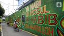 Warga berjalan di depan mural bernuansa Islami di Gang Pelangi, kawasan Kalibata, Jakarta, Jumat (23/4/2021). Mural bernuansa Islami tersebut dibuat warga untuk menghiasi dan meramaikan pintu masuk gang dalam rangka menyambut bulan Ramadhan. (Liputan6.com/Herman Zakharia)