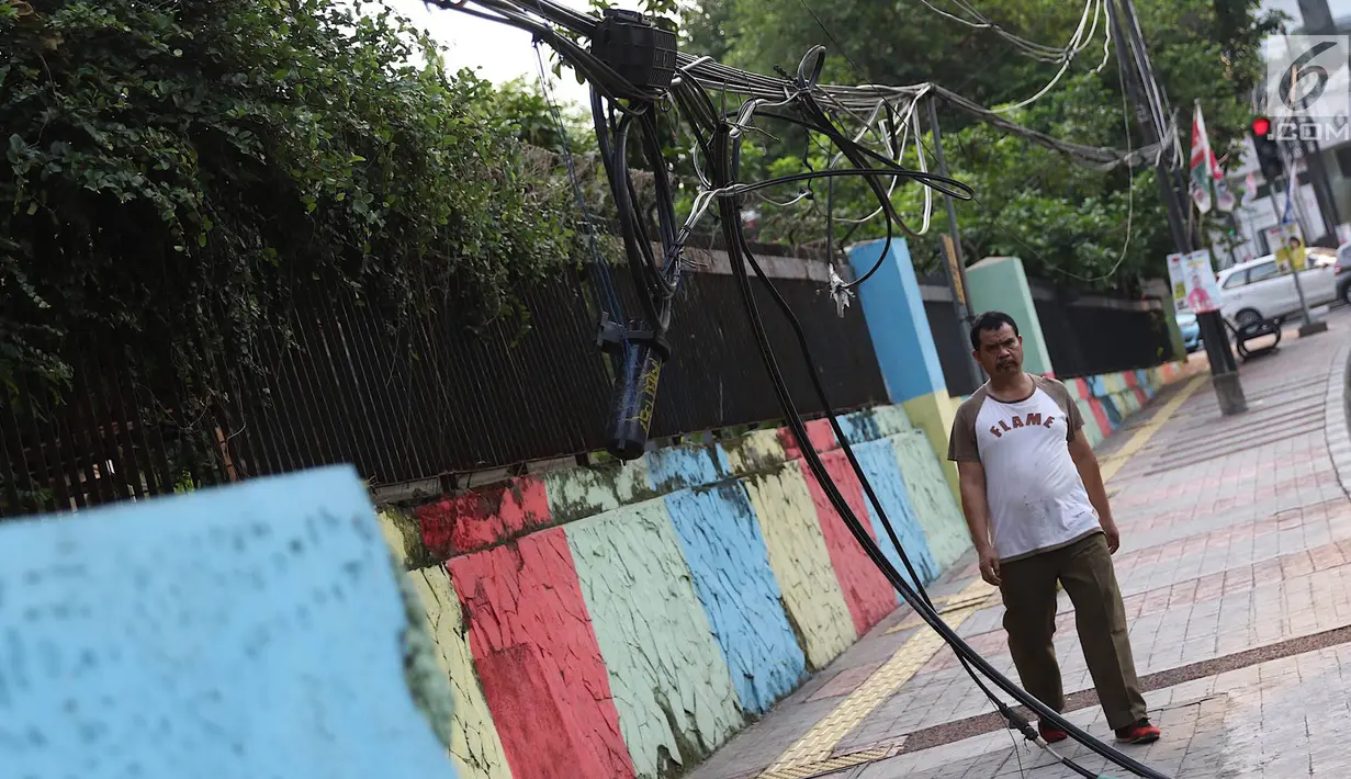 Pejalan kaki melintasi trotoar yang terhalang instalasi kabel di Jalan Kyai Maja, Jakarta, Rabu (10/4). Selain menganggu kenyamanan pejalan kaki, kondisi instalasi kabel yang semrawut tersebut juga berbahaya apabila mengandung aliran listrik. (Liputan6.com/Immanuel Antonius)