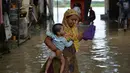 Seorang wanita membawa seorang anak saat melintasi banjir di daerah perumahan dekat tepi Sungai Yamuna yang meluap di New Delhi, India, Selasa (20/8/2019). (AFP Photo/Sajjad Hussain)