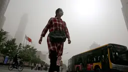 Seorang wanita berjalan sambil mengenakan masker saat badai debu menerjang kota Beijing, China, Kamis (4/5). Badai debu membuat otoritas memerintahkan orang tua dan anak-anak untuk tetap berada dalam ruangan. (AP Photo/Andy Wong)
