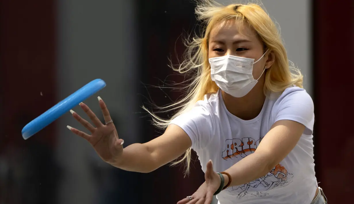 Seorang wanita yang mengenakan masker bermain dengan frisbee di Beijing, China, 13 April 2022. Shanghai bergerak untuk lebih melonggarkan lockdown di kota terbesar di China tersebut yang tampaknya terhenti. (AP Photo/Mark Schiefelbein)