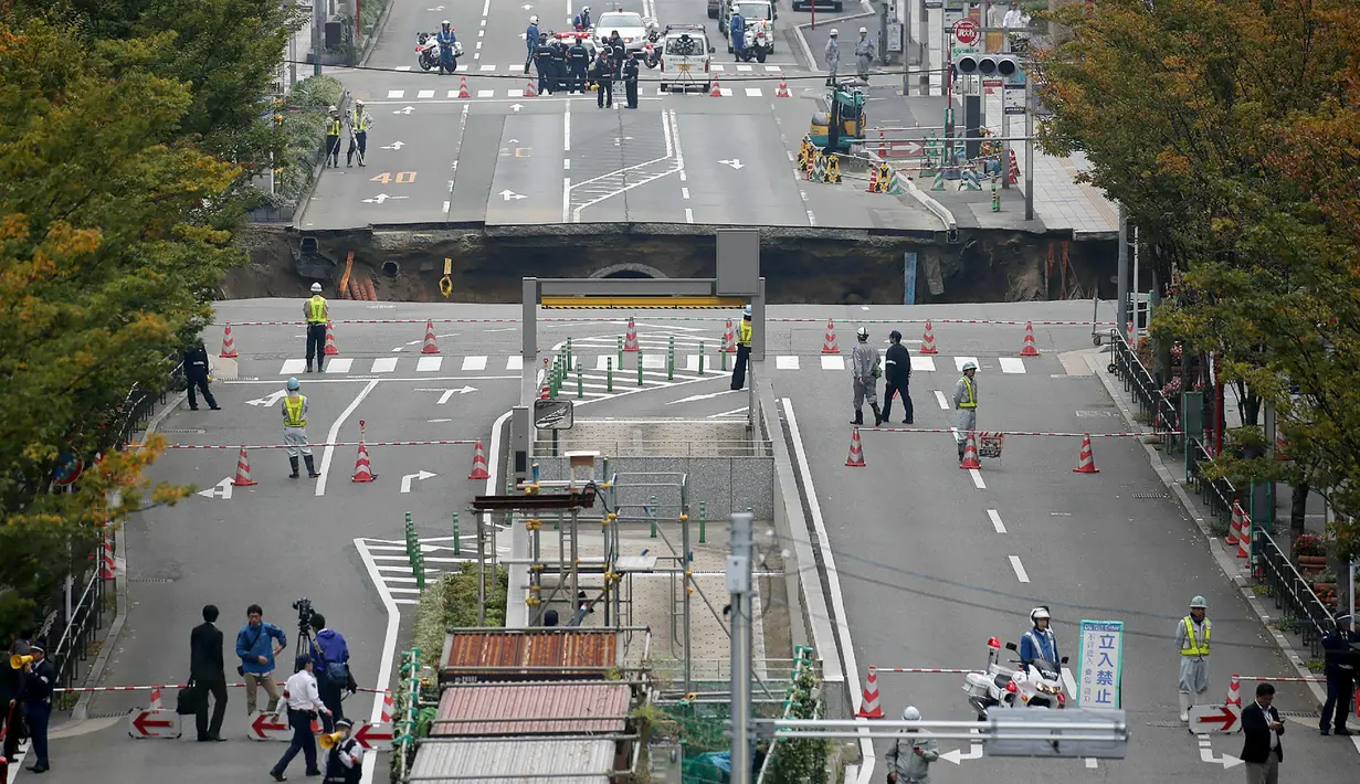 Sejumlah petugas mengamankan lokasi munculnya sebuah lubang raksasa atau yang biasa disebut sinkhole di persimpangan dekat Stasiun Hakata, Fukuoka, Jepang, Selasa (8/11). Jalanan itu tiba-tiba runtuh hingga menciptakan lubang besar. (STR/JIJI PRESS/AFP)