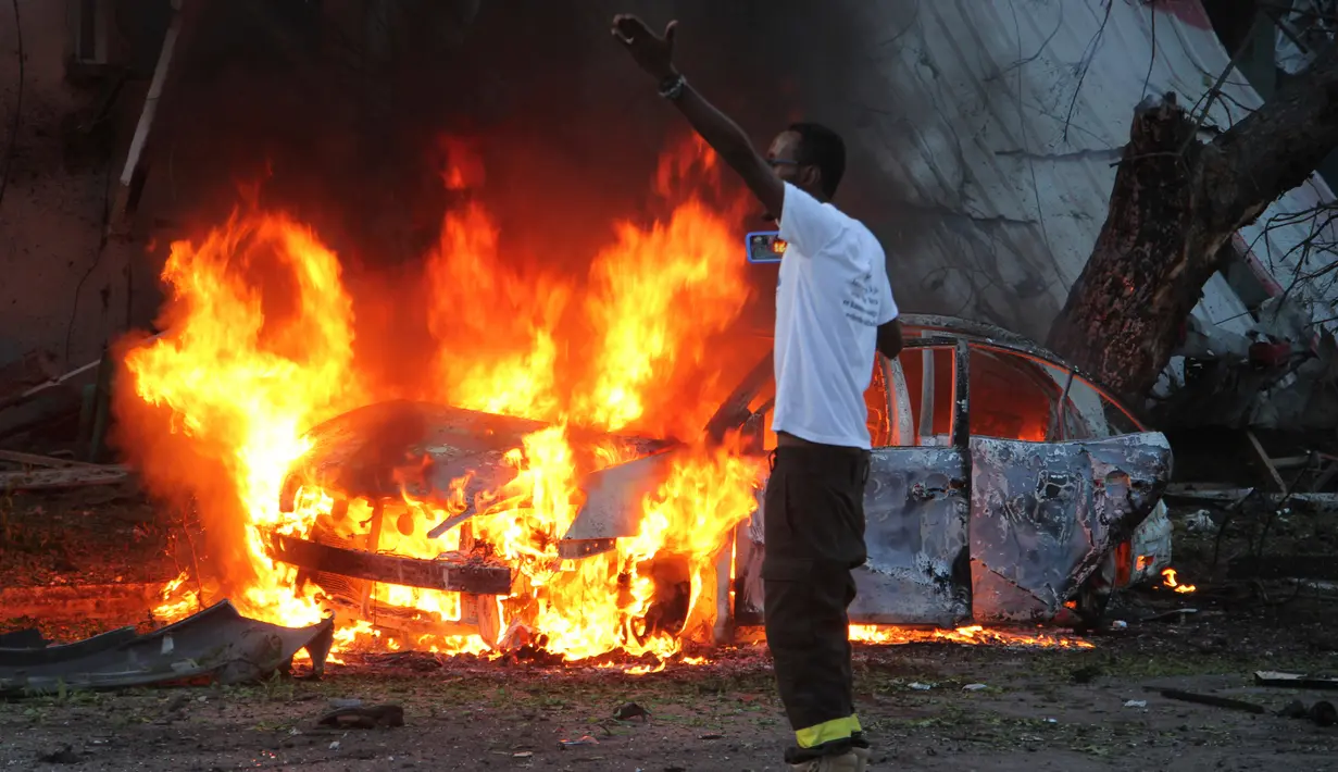 Seorang pria berdiri di dekat sebuah mobil yang terbakar setelah sebuah serangan bom di sebuah restoran di Mogadishu, Somalia (8/5). Setidaknya 6 orang tewas dan 10 orang lainnya terluka dalam serangan bom mobil tersebut. (AP Photo/Farah Abdi Warsameh)