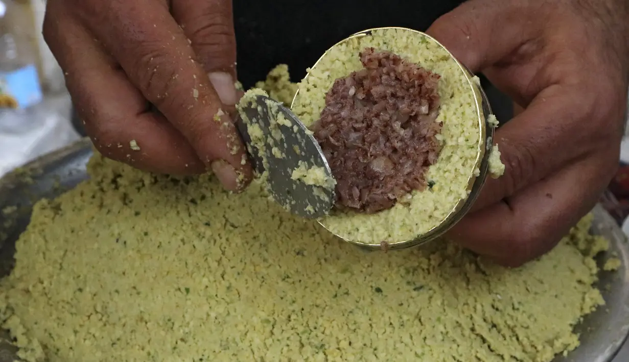 Seorang pedagang Palestina menyiapkan falafel diisi dengan bawang, sumac dan cabai, di restoran lokal di kota Hebron di Tepi Barat yang diduduki, Minggu (18/4/2021). Falafel adalah sebuah makanan Timur Tengah yang pada bulan Ramadhan, sering dimakan sebagai hidangan buka puasa. (HAZEM BADER/AFP)