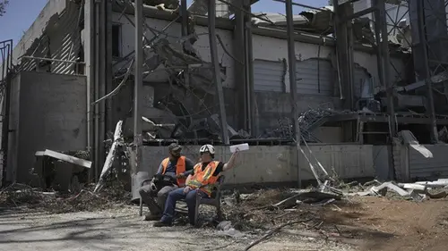 Para pekerja duduk di samping sebuah gedung di Institut Sains Weizmann di Rehovot, Israel, yang hancur akibat rudal Iran Kamis (19/6/2025).
